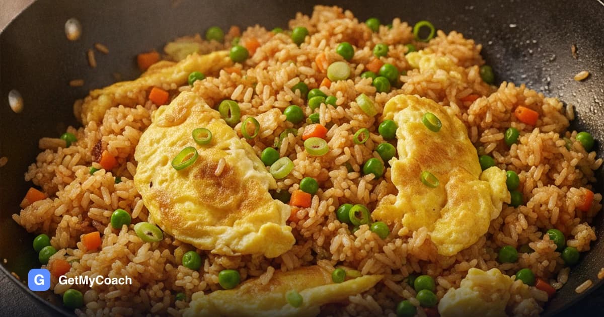A pan of golden fried rice with folded pieces of scrambled egg, green peas, diced carrot and sliced spring onion.