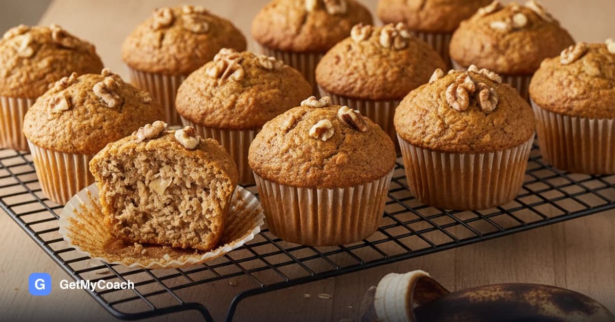 Twelve golden-brown muffins in paper cases cooling on a wire rack, studded with walnut pieces, one split open to show a moist, dense crumb.