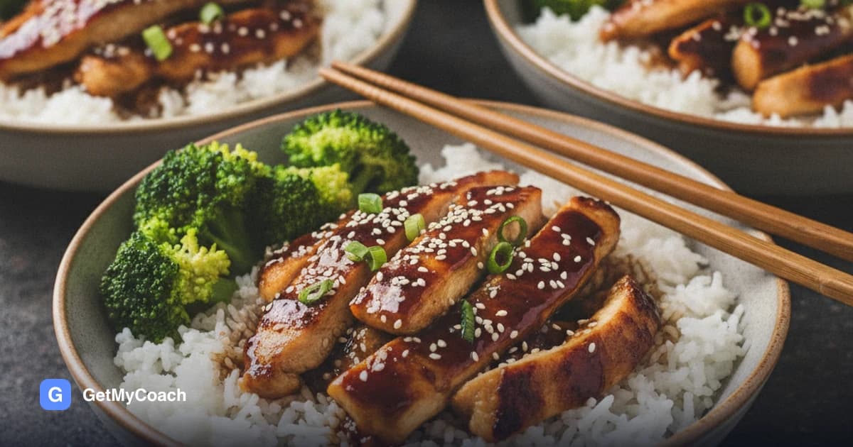 A bowl of jasmine rice topped with glazed teriyaki chicken strips, bright green broccoli florets, sesame seeds and sliced spring onion, with three more bowls out of focus behind it.